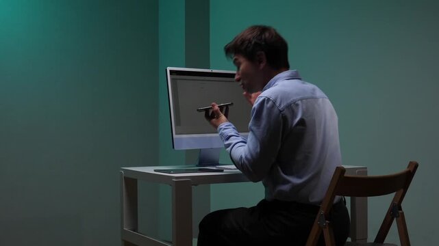 Man in a corporate environment dealing with technical difficulties and work related pressure, sitting at a desk and shouting angrily into his smartphone near a computer