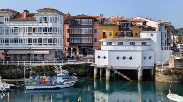 A fishing boat docked beside the fish market (lonja) building on stilts in the harbor of Llanes, Asturias