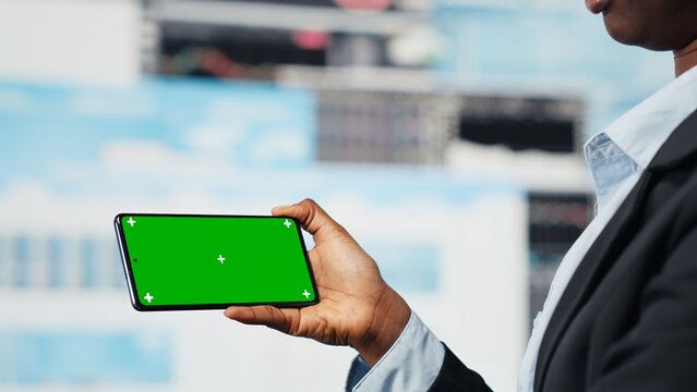 Manager uses an isolated-screen smartphone to compare company metrics on a digital videowall before making decisions, while an entrepreneur analyzes key performance indicators with a mockup phone.