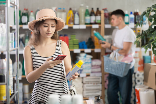 Girl buyer scans qr code on mosquito repellent label, uses link to get additional information on Internet. Customer photographs product, searches for photo on Internet, man shopping in background
