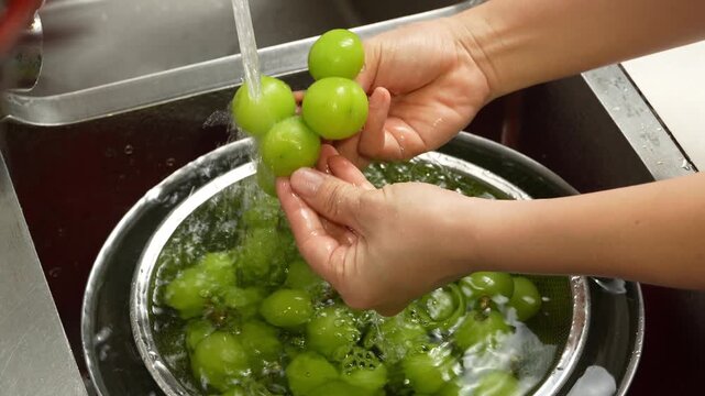 Close-up of hands washing fresh green grapes in water colander under kitchen tap.