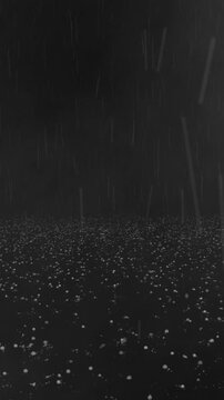 Vertical video of hail and rain falling and bouncing on a dark floor surface.