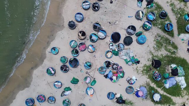 Top down aerial drone perspective capturing geometric pattern of blue round traditional Vietnamese coracle fishing basket boats parked on sandy beach shore in Mui Ne bay near Phan Thiet.