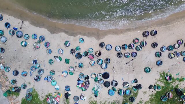 Top down aerial drone perspective capturing geometric pattern of blue round traditional Vietnamese coracle fishing basket boats parked on sandy beach shore in Mui Ne bay near Phan Thiet.