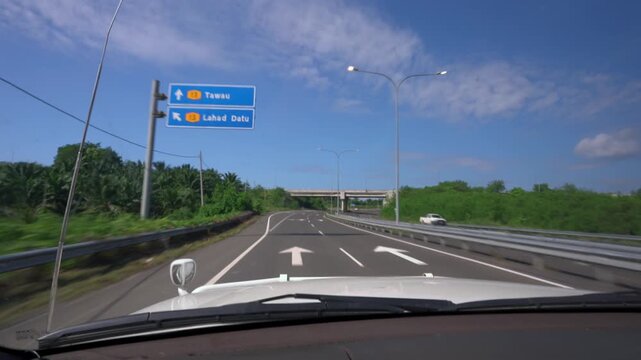 Fixed dashboard view from a moving car on a divided highway in Sabah, passing road signs directing traffic toward Tawau and Lahad Datu.