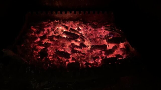 4k slowly moving forward footage of burning red chunks of wood inside a chimney with flying sparks and small flames, after hours of active fire
