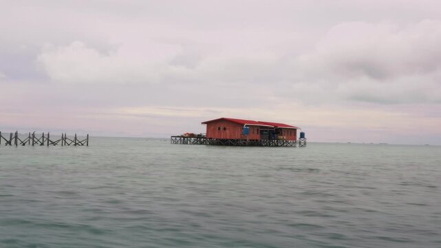 A fast-moving boat passes a remote stilt house built over shallow sea water, with motion blur visible across the foreground and supporting structures.