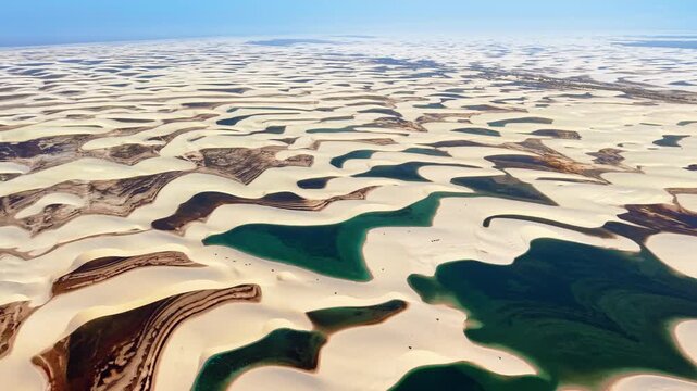 High-altitude aerial drone view of long white dune ridges with narrow blue lagoons between them, Lencois Maranhenses, Brazil