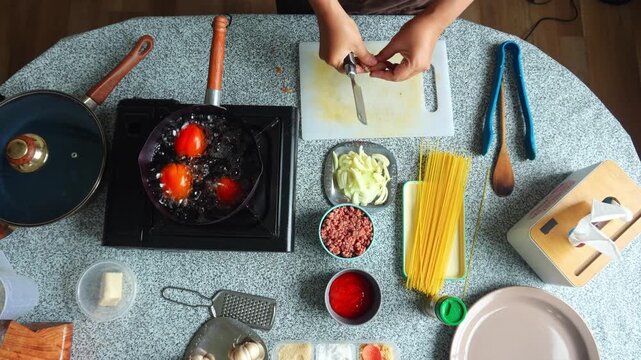 Top-down view of chef peeling garlic cloves on cutting board surrounded by spaghetti ingredients
