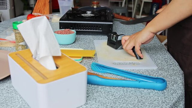 Hands sharpening knife with handheld sharpener on table prepared for cooking