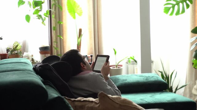 Young man reading an e-book relaxing on a green sofa