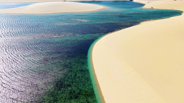 Aerial drone view of white sand dunes and a wide green lagoon under the afternoon sun, Lencois Maranhenses, Brazil