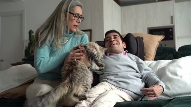 Mother and disabled son playing with cat on sofa