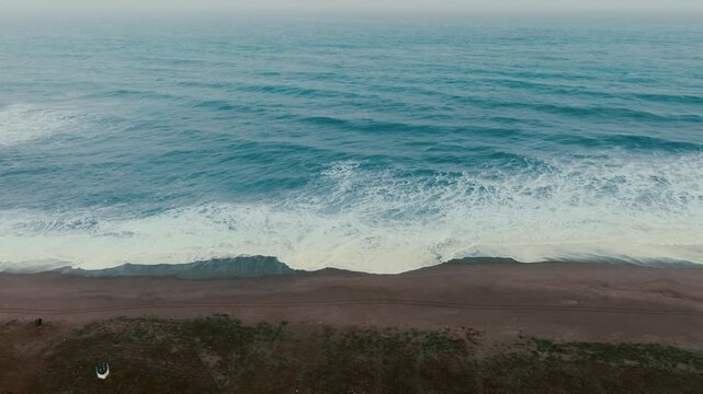 Long, repetitive ocean waves on sandy beach in the evening aerial