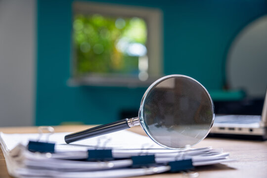Shown are documents held together with paper clips and a magnifying glass. Office Business