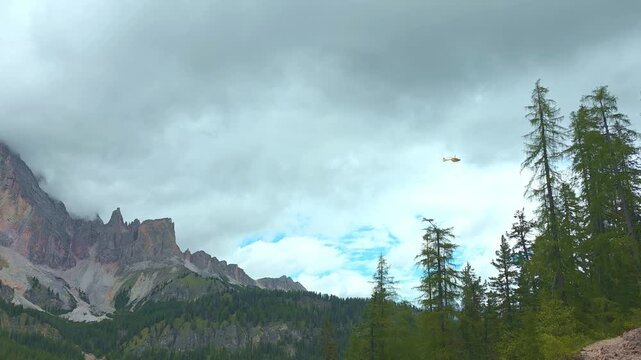 Yellow rescue helicopter flying low surrounded by the dramatic rocky peaks of the Italian Dolomites