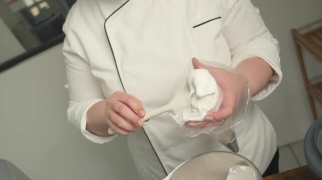 Close-up of a pastry chef filling a piping bag with meringue for decorating lemon tartlets.
