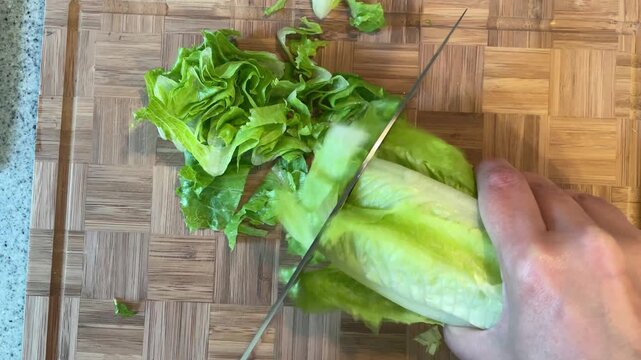Close up overhead of sharp knife slicing crisp romaine lettuce into thin ribbons on cutting board