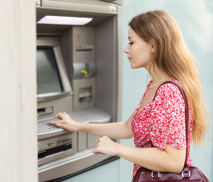 Young woman carefully enters the pin code from the card at the atm, so that no one sees. European woman withdraws cash from the card