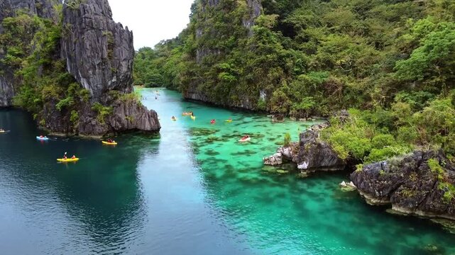 Aerial drone view of kayaks crossing the clear green water of a large lagoon between limestone cliffs, El Nido, Philippines
