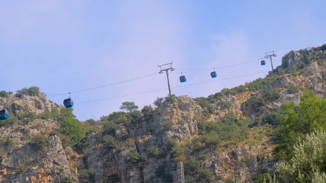 Ropeway and cable car cabins moving against cloudy sky over Mount Babadag in Mugla, Turkey. Aerial rope transit, gondola lift, view from the foothills. Tourism, sightseeing, and transportation concept