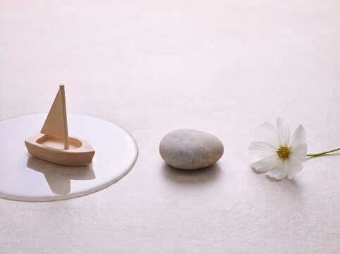 Zen still life, wooden toy boat on mirror, smooth stone and white flower