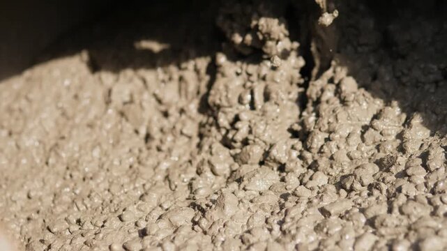 Thick concrete slurry fills container with chunky lumps, glossy moisture, and rough granular texture under strong shadow, with concrete, cement, slurry, wet detail, showing chunky, clump, settling