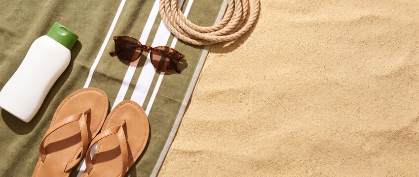 A sun-drenched beach scene features essential summer vacation accessories, including a bottle of sunscreen, sunglasses, flip-flops, and a rolled-up towel, all artfully arranged on soft, golden sand.