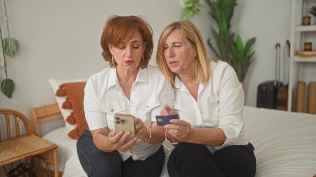 Woman holding smartphone and creditcard on bedroom bed, hands tapping screen and leaning close together; online payment concern.