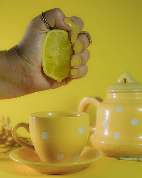 Mano exprimiendo medio lim&oacute;n sobre una taza amarilla con fondo amarillo.