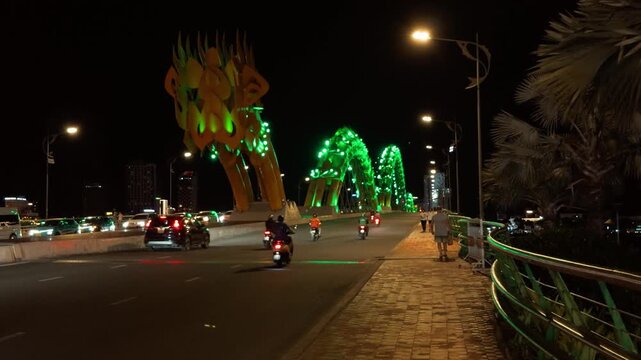 Dragon bridge in da nang, vietnam, glowing with vibrant green lights at night as pedestrians stroll the waterfront and traffic creates light trails across the han river