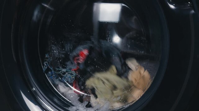 Front loading washing machine drum full of colorful clothes tumbling in soapy water and foam, close up of an efficient wash cycle showing motion, bubbles and freshness