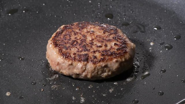 Grilled hamburger steak patty with seared crust cooking on a black griddle, camera zooms in and pans across the surface