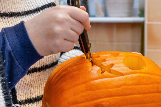 Hand carving mouth on orange Halloween pumpkin with knife
