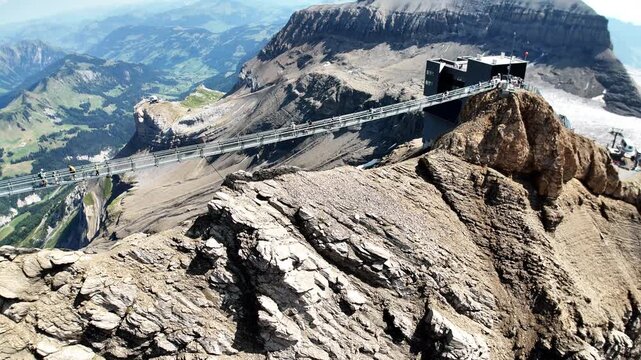 Scenic footage of the Peak Walk suspension bridge connecting two mountain peaks at Glacier 3000 in the Swiss Alps, with visitors crossing the high-altitude bridge surrounded by dramatic alpine scenery