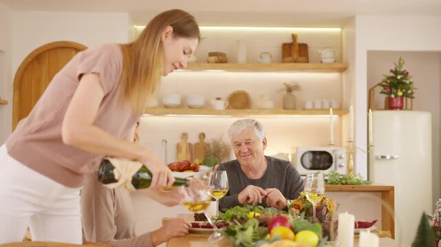 Senior parents and adult daughter enjoy Christmas dinner together at home. Happy family sharing festive holiday meal with roast chicken, salad and wine around dining table during seasonal celebration.