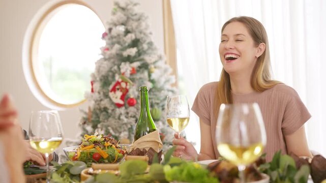 Senior parents and adult daughter enjoy Christmas dinner together at home. Happy family sharing festive holiday meal with roast chicken, salad and wine around dining table during seasonal celebration.