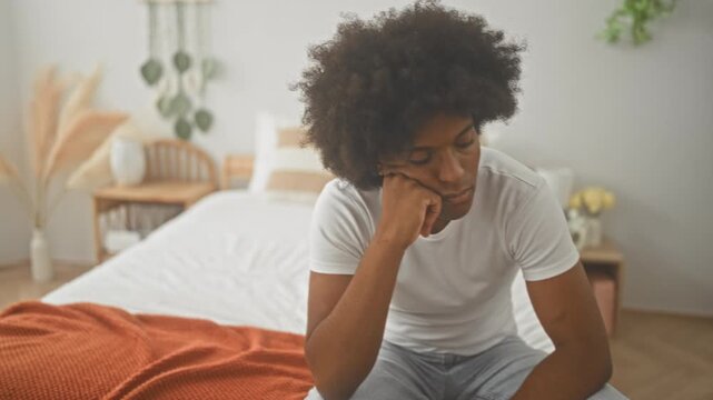 Two african american men sit on bed, one resting chin on hand while the other leans in and gestures with hand, bedroom; sadness support empathy.