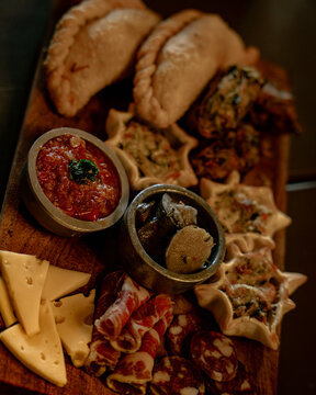 Tabla de picada r&uacute;stica con empanadas, fiambres, quesos y salsas.