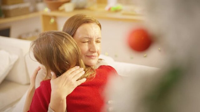 Family Christmas festive holiday celebration. Adult daughter hug senior mother on sofa at home. Happy Caucasian women sharing emotional special moment with family and seasonal tradition celebrating