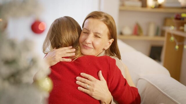 Family Christmas festive holiday celebration. Adult daughter hug senior mother on sofa at home. Happy Caucasian women sharing emotional special moment with family and seasonal tradition celebrating