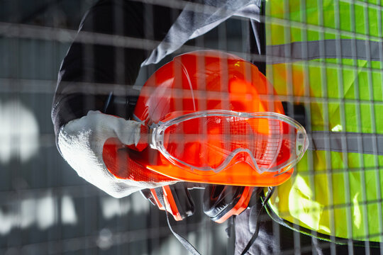 Construction worker holding hard hat and safety goggles at industrial site. Protective equipment, workplace safety and construction industry concept.