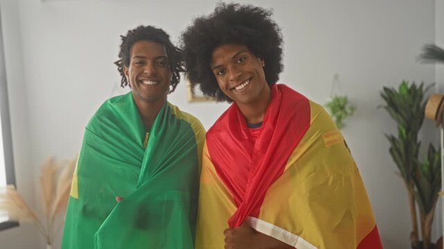 Man holds national flags over shoulders and smiles wearing brazil and spain soccer jerseys inside a building during a match as supporters; team spirit joy.