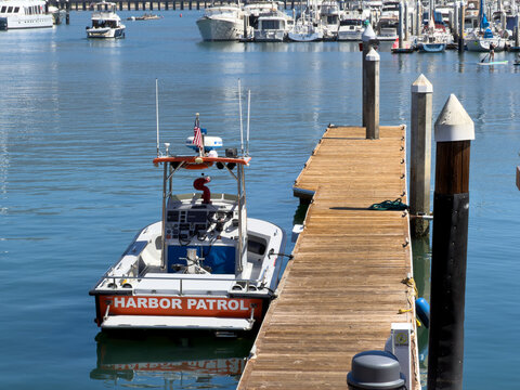 SANTA BARBARA, CA, APR 8, 2026: Rear view of Harbor Patrol boat docked beside pilings, with a paddle boarder and marina boats in the background