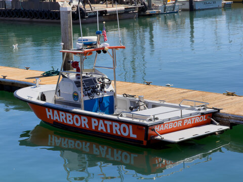 SANTA BARBARA, CA, APR 8, 2026: Side-angled view of a Harbor Patrol boat with lettering on its side and rear, docked among tire-bumpered barges