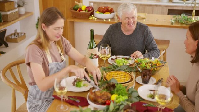 Senior parents and adult daughter enjoy Christmas dinner together at home. Happy family sharing festive holiday meal with roast chicken, salad and wine around dining table during seasonal celebration.