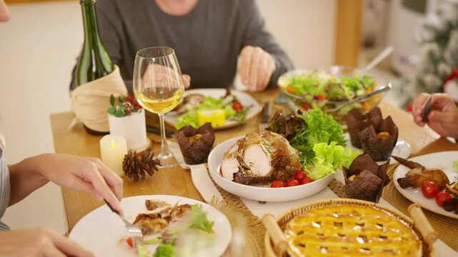 Senior parents and adult daughter enjoy Christmas dinner together at home. Happy family sharing festive holiday meal with roast chicken, salad and wine around dining table during seasonal celebration.