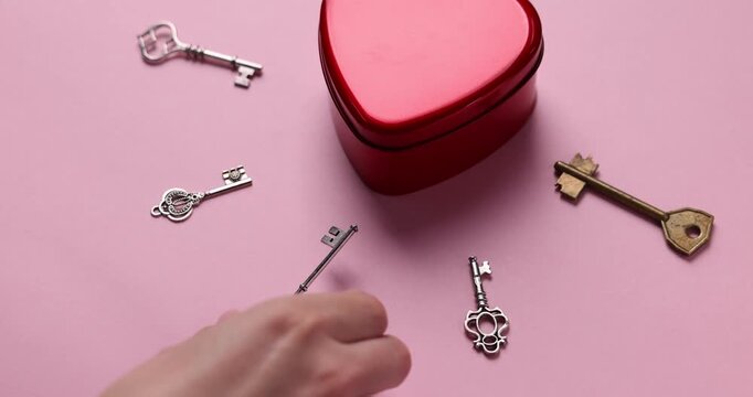 Woman choosing key to heart shaped box on pink background, closeup