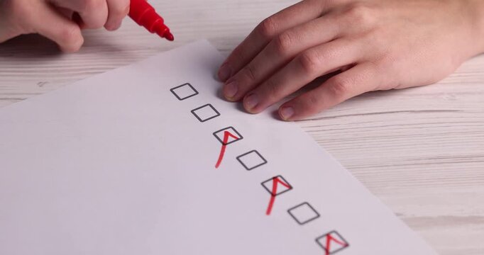Choice concept. Woman putting check marks into boxes on paper sheet at wooden table, closeup