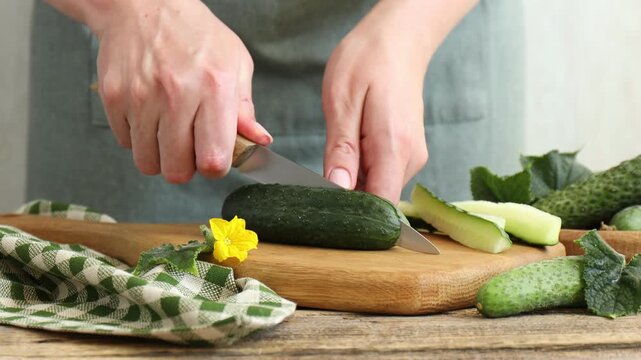 Woman cutting cucumber at wooden table, closeup